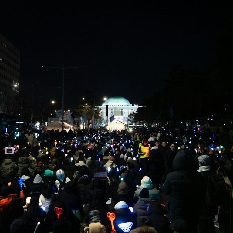 A night crowd outside Korea's National Assembly holding glowing K-pop light sticks