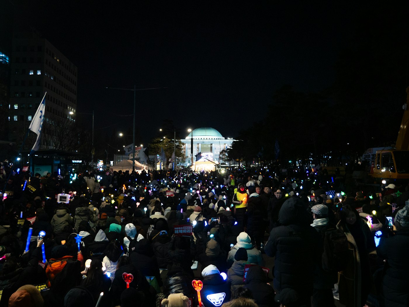 A night crowd outside Korea's National Assembly holding glowing K-pop light sticks