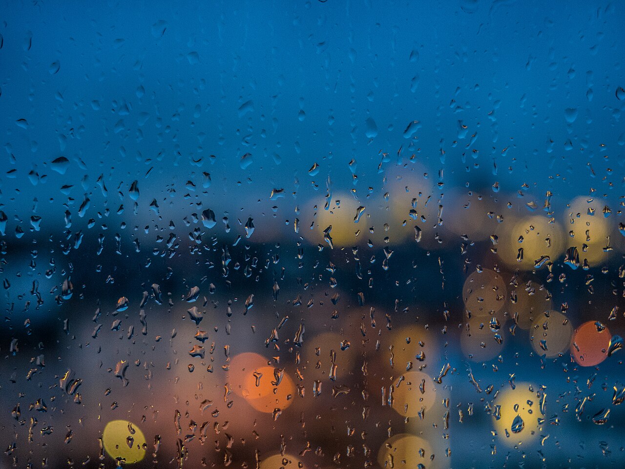 Raindrops on a window pane at dusk, city lights blurred behind