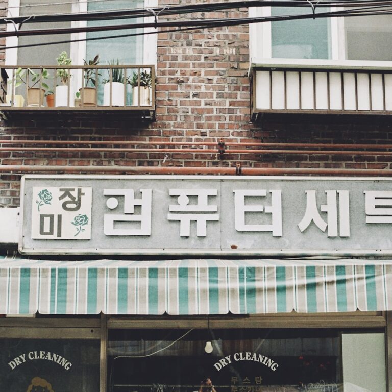 An old Korean dry-cleaning shopfront in a brick building, with plants on the balcony above