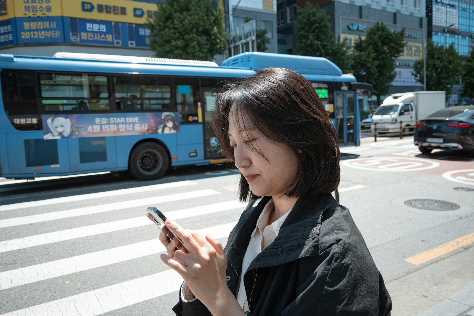 A woman checking her phone at a crosswalk in Seoul